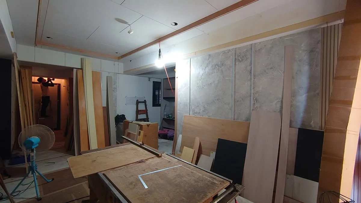 工地現場堆放大量板材與裁切工作台,牆面貼覆灰色大理石紋板