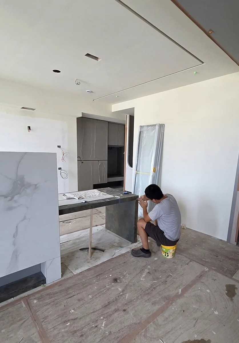 施工中的廚房，大理石紋中島立板已就定位，師傅蹲在中島旁安裝