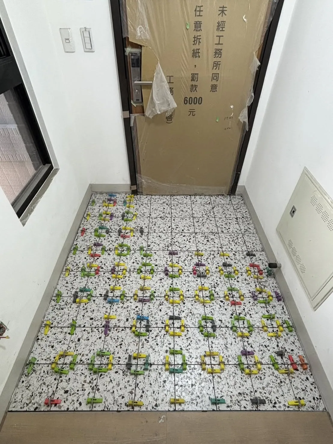 玄關地面鋪貼磨石子紋磁磚,磚縫夾著彩色整平器尚未拆除