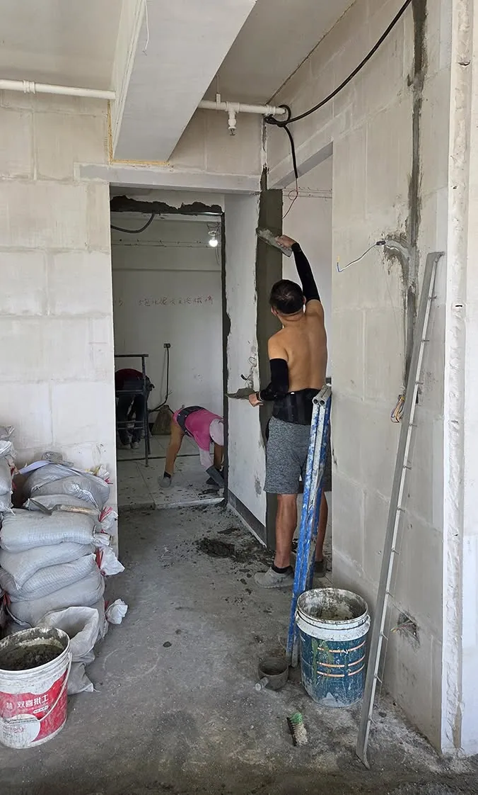 工作人員在室內牆面前檢視結構與防水狀況,牆面已局部打除露出結構層