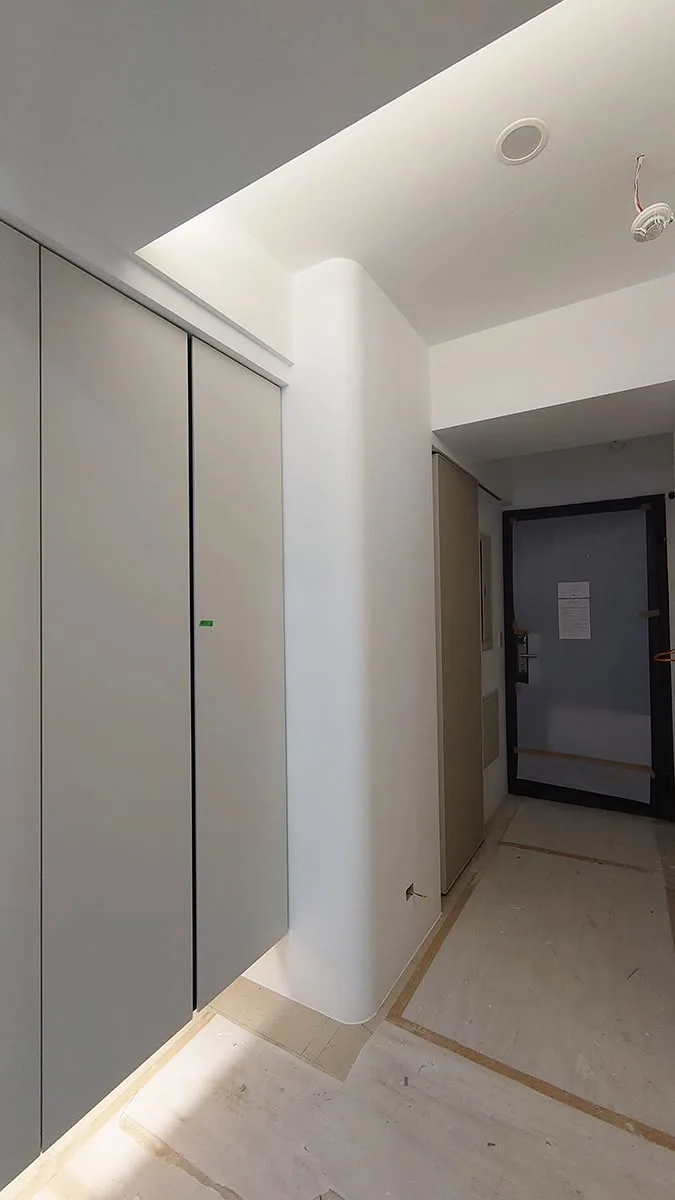 接近完工的玄關走道，左側為整排白色門片櫃體與圓弧轉角牆，地面仍鋪保護板
