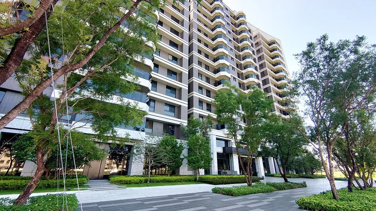 社區大樓外觀為米色磚紅立面,弧形陽台層層堆疊,中庭有草坪與喬木景觀
